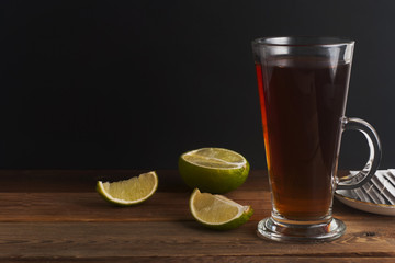 Glass Cup ofblack tea with lime, close up on rustic wooden background. Warm autumn or winter drinks.