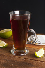 Glass Cup ofblack tea with lime, close up on rustic wooden background. Warm autumn or winter drinks.