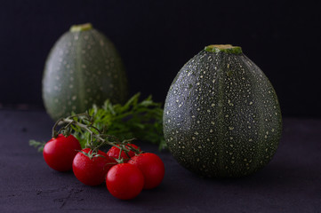 Two fresh Round Zucchini's (Rondini) and cherry tomatoes on black background. Low key