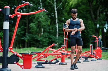 African american male athlete sport man with running sports arm case for mobile phone, posed against street workout simulators.