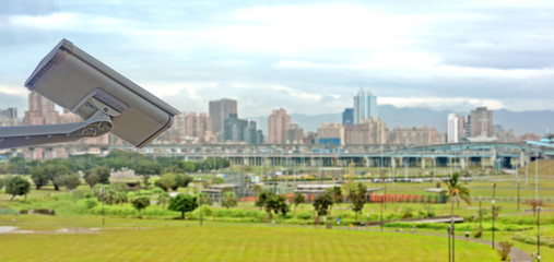 CCTV closed circuit camera in landscape of city with lots of buildings and park on the background