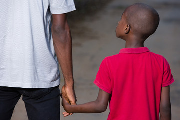 father and little son holding hands walking on a road.