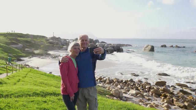 Senior couple taking selfies overlooking the sea