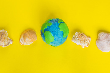 Travel concept, plasticine earth and seashells on the yellow background.
