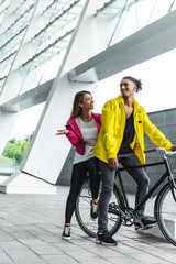 young smiling multicultural couple sitting on bicycle at city street