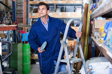 Man in unifom is using ladder to reach the top shelves in the building store.
