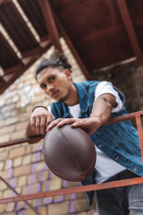 selective focus of mixed race man showing rugby ball at urban street