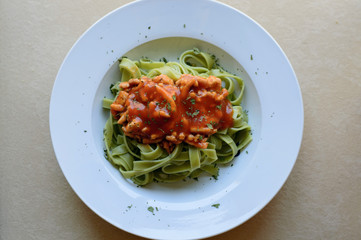 Primer plano de un plato de tallarines de espinaca con carne y salsa de tomate a lo boloñesa en un plato blanco con orégano ara decorar