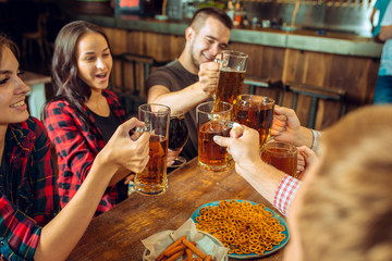 people, leisure, friendship and communication concept - happy friends drinking beer, talking and clinking glasses at bar or pub