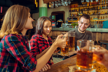people, leisure, friendship and communication concept - happy friends drinking beer, talking and clinking glasses at bar or pub