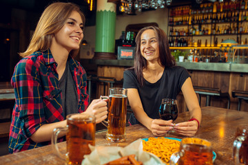 people, leisure, friendship and communication concept - happy friends drinking beer, talking and clinking glasses at bar or pub