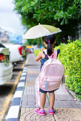 little girl with umbrella and backpack walking in the park ready back to school in raining day