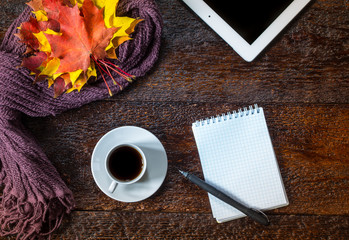 Still life of cup of coffee, scarf,autumn leaves, notepad, pen and tablet on brown wooden background