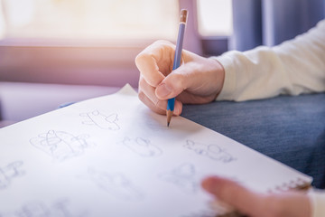 Woman performs free-hand pencil drawing the artworks on white paper in soft tone of warm light from window.