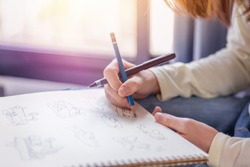 Woman performs free-hand drawing the artworks by pen and pencil on white paper in soft tone of warm...