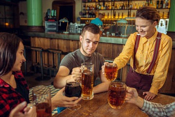 people, leisure, friendship and communication concept - happy friends drinking beer, talking and clinking glasses at bar or pub