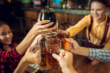 people, leisure, friendship and communication concept - happy friends drinking beer, talking and clinking glasses at bar or pub