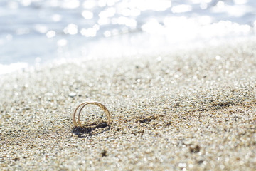 Pair of gold wedding rings on sand beach by sea