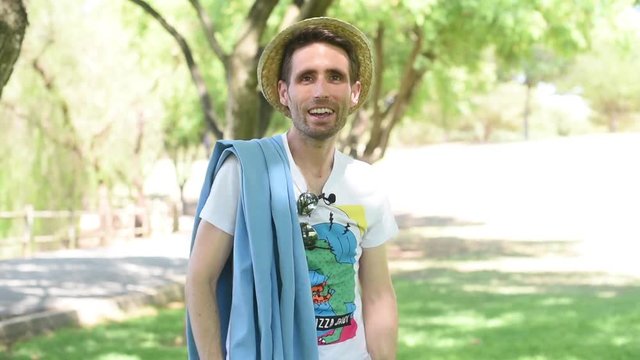 Hombre joven vestido con ropa veraniega, con sombrero y toalla, bailando divertido y ri&eacute;ndose.