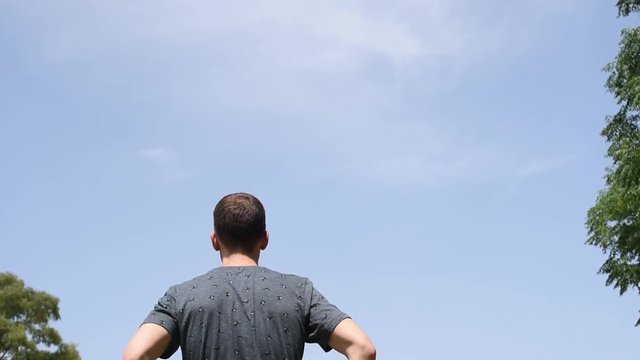 Hombre con camiseta azul de espaldas bajo dielo azul despejado al aire libre en la naturaleza.
