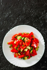 fresh vegetable salad with tomato, cucumber and green onion in white plate on black background. with copy space. top view