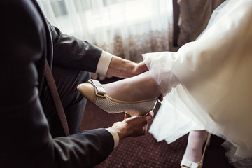 Obraz na płótnie Canvas groom dresses on the bride's foot wedding shoe