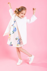 A teenage girl in light clothes posing on a pink background.