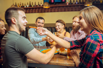 people, leisure, friendship and communication concept - happy friends drinking beer, talking and clinking glasses at bar or pub