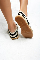 Cropped back view of woman's legs in striped espadrille shoes, isolated on a white background....