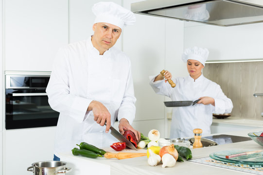 Two positive female and male young cooks wearing uniform working