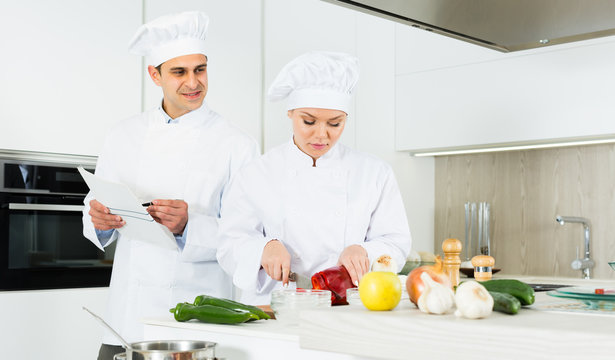 Woman and man professionals are cooking salad in the kitchen