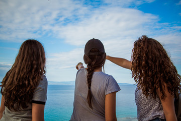 Rear view of girls standing on cliff and looking at the horizon  / Looking at view and pointing