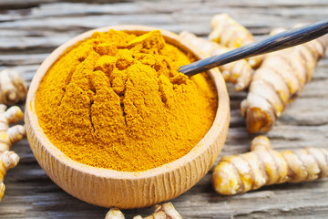 Turmeric powder in bowls and fresh turmeric on old wooden background.
