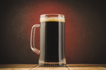 mug full of beer on a red light background/mug full of beer on a wooden table and a red light   background, selective focus