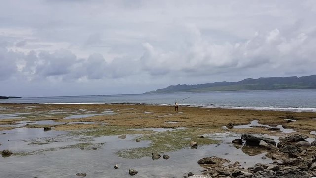 An Ivatan fisherman walking along the shore during low tide holding a tradition tool for fishing. Shot on Basco, Batanes - Philippines.