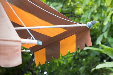 brown and yellow striped awning in tropical garden background after raining. - obrazy, fototapety, plakaty