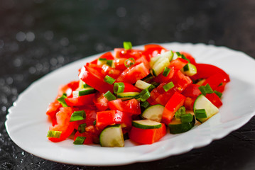 fresh vegetable salad with tomato, cucumber and green onion in white plate on black background.