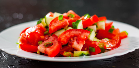 fresh vegetable salad with tomato, cucumber and green onion in white plate on black background.