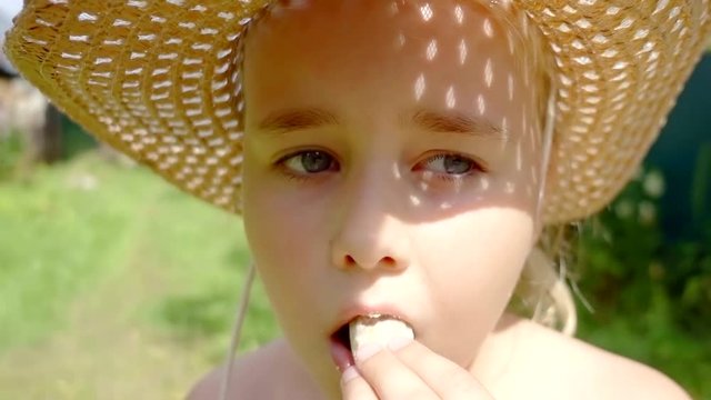 Portrait of a beautiful little girl in hat eating a snack outside in summer.