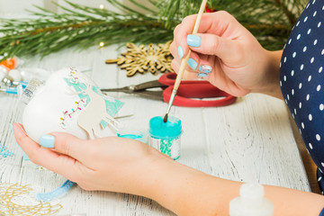 Christmas decorations, balls, toys and gift boxes on an old wooden board. Female hands make Christmas decorations