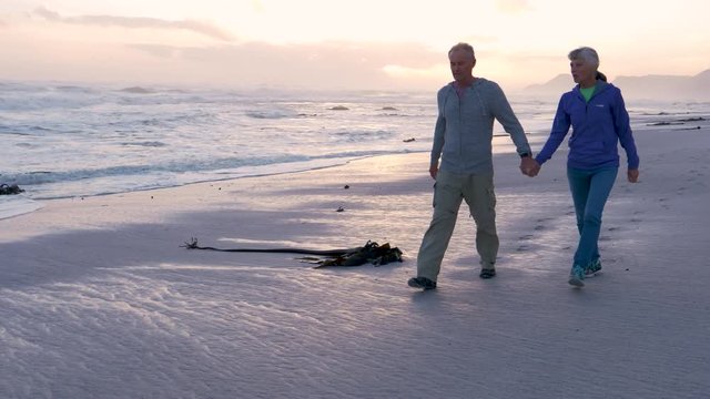 Senior couple walking at sunset on a sandy beach 