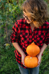 Woman is standing in the garden and holding orange pumpkins in her hands. Season harvesting. 