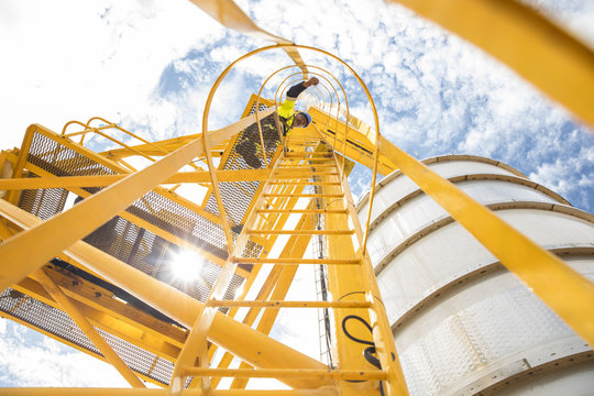 Worker on ladder by storage tank