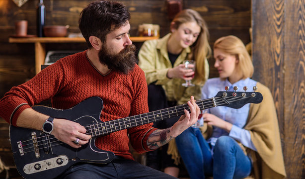 Girls listening to song performed by handsome bearded musician. Guitarist entertaining guests at party. Man with hipster beard playing electrical guitar. Bearded man united with his instrument
