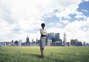 Camera headed woman standing on green grass against modern citys