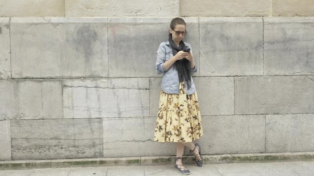 4 k beautiful young girl in jeans jacket, yellow broad skirt typing mobile phone at the old european street