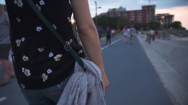 Woman's purse and sweater hanging by her side as she walks path at dusk