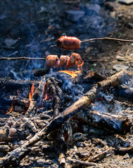 How to roast sausages. Sausages on stick with bonfire and smoke on background. Roasty toasty sausages are such quintessential taste of picnic. Holding sausages on sticks. Smoky smell of roasted food
