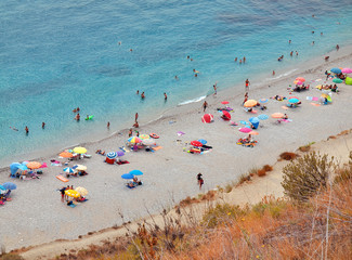 Strandabschnitt am Mittelmeer mit Urlaubsgästen unter bunten Sonnenschirmen