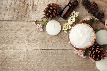 Spa and wellness setting with sea salt, oil essence, cones and candle on wooden background. Fall...